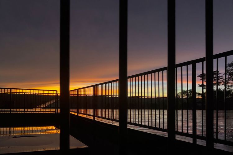 Silhouette bridge over river against sky during sunset