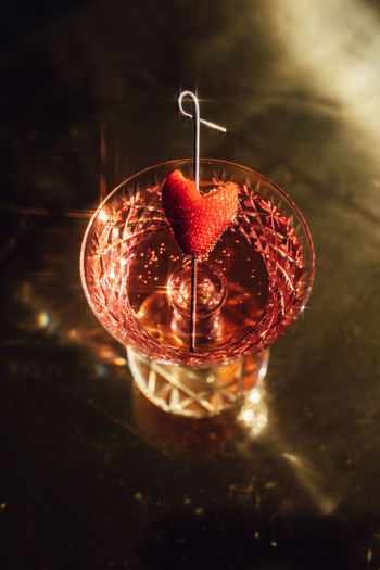 Pink sparkling wine drink in cut crystal champagne coupe with strawberry heart garnish on brass 