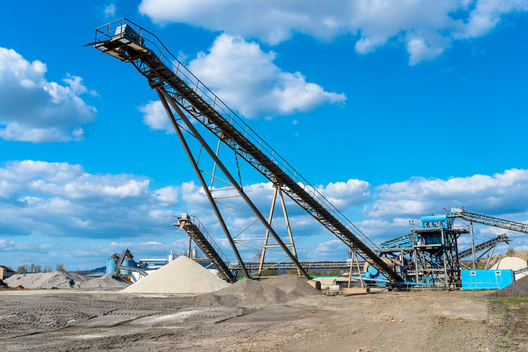 Conveyor over heaps of gravel on blue sky at an industrial cement plant.