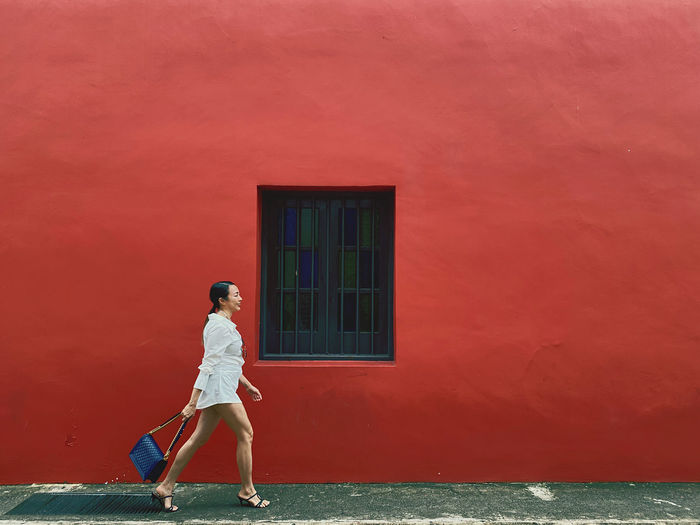 Full length side view of woman walking against red wall outdoors