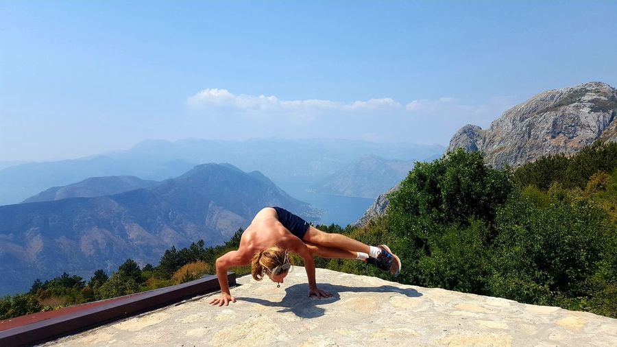 Shirtless man exercising at observation point by mountains against sky