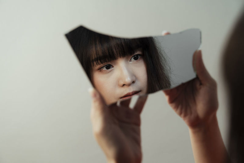 Woman holding mirror against wall