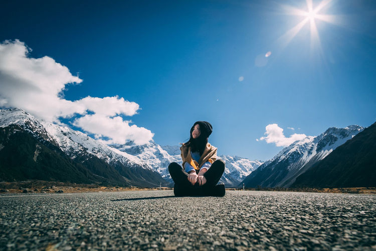 Young woman sitting on snowcapped mountain against sky