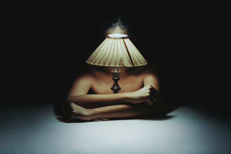Shirtless woman sitting with illuminated lamp on table in darkroom