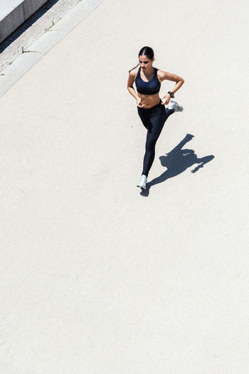 From above of fit female in sportswear running fast along pavement during training on sunny day in city