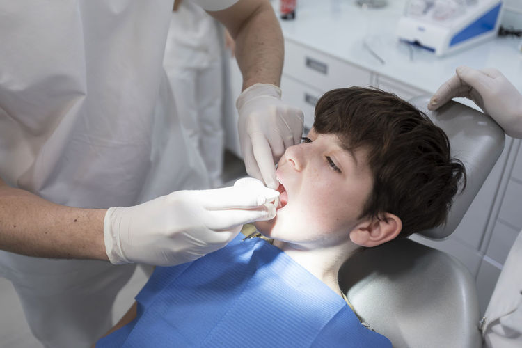 Midsection of dentist examining boy tooth in clinic