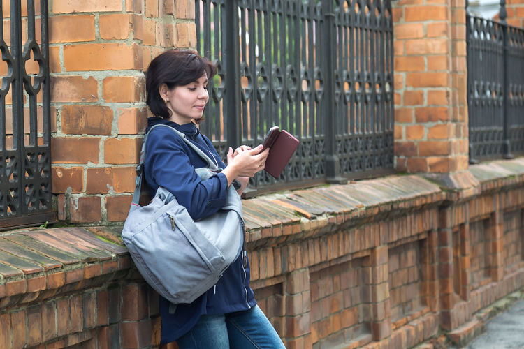 A brunette woman on the street with a smile looks into the phone texting with her lover.