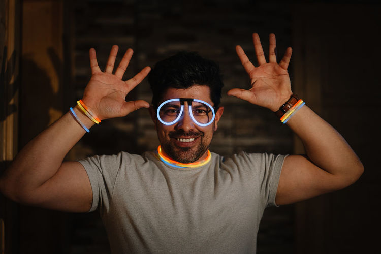 Portrait of young man wearing neon glasses smiling and gesturing at home