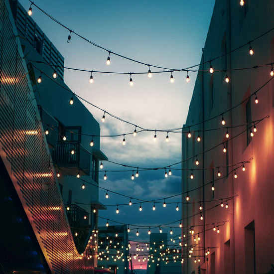 Low angle view of illuminated light bulbs amidst building against sky at night