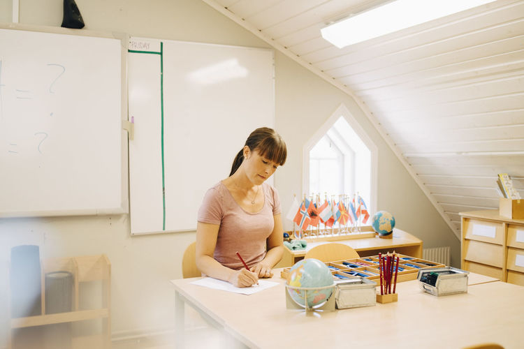Mid adult teacher writing at desk while sitting in classroom