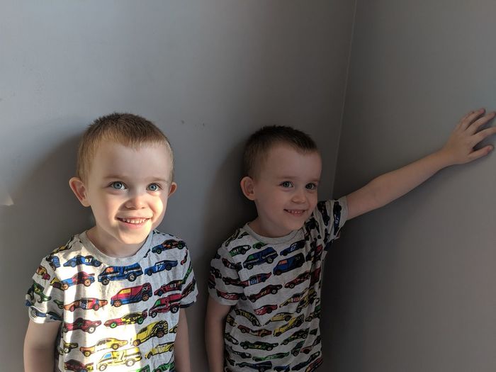 Smiling brothers looking away while standing against wall at home
