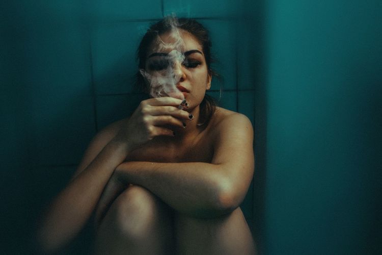 Naked woman smoking cigarette against wall