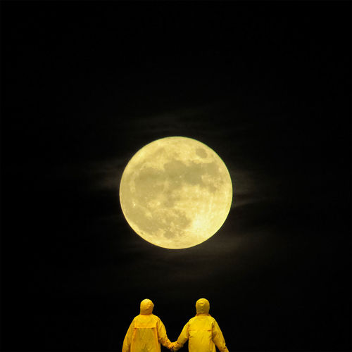 Rear view of people wearing yellow raincoats looking at moon against clear sky during night