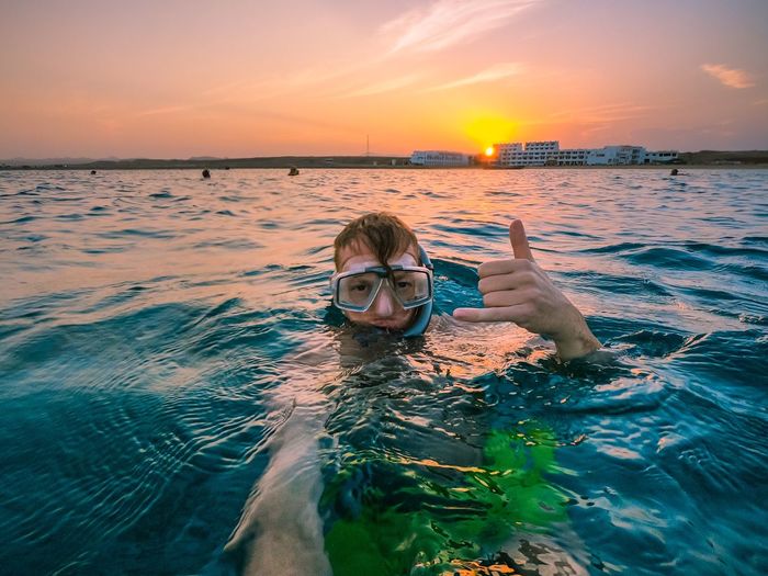 Portrait of man gesturing while swimming in sea during sunset