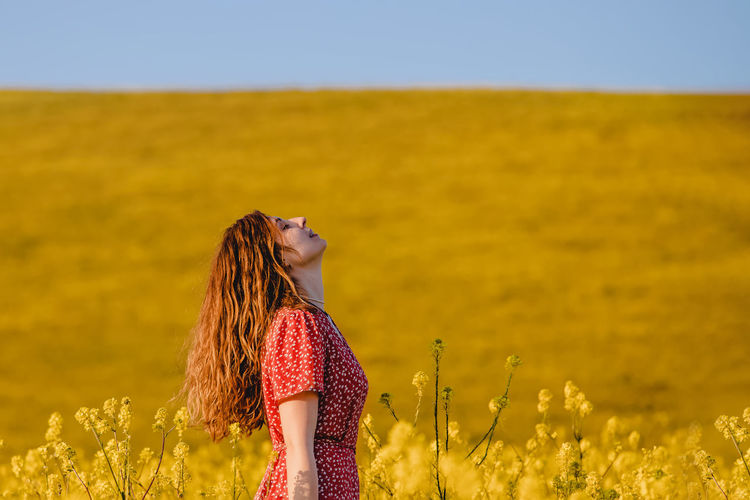 Portrait of young woman enjoying warm spring sunny weather outdoors in the blooming mustard field