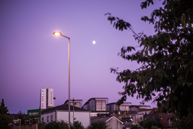 Low angle view of illuminated street lights against sky at dusk