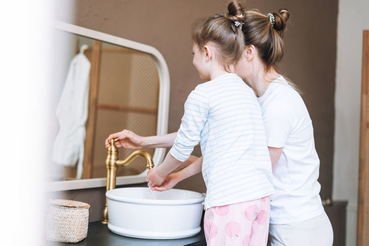 Young mother woman with little girl daughter in pajamas washing face and hands in at home