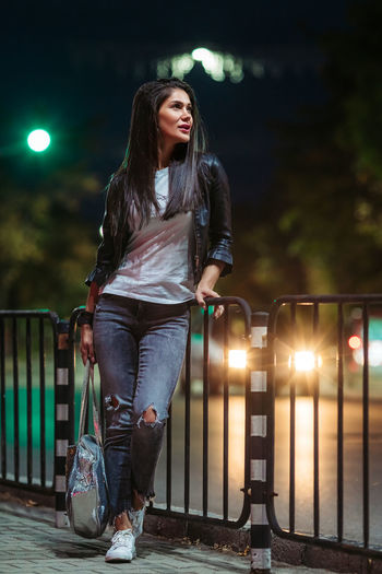Beautiful woman standing by railing at night on road