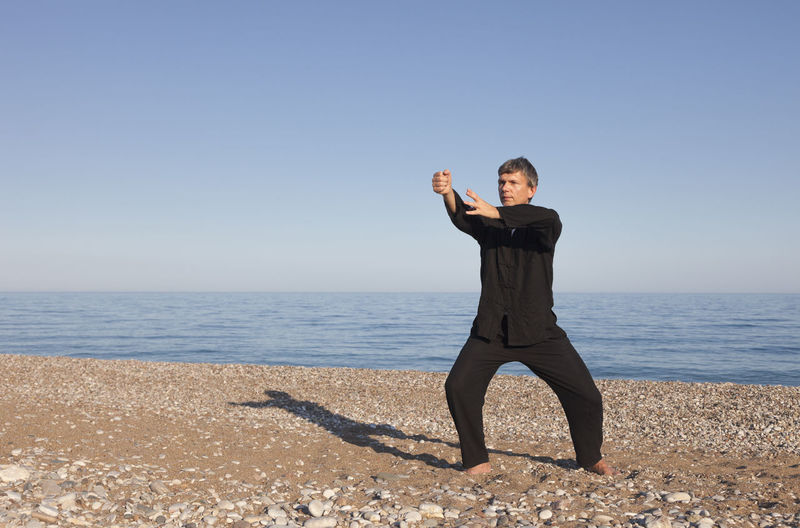 Man practicing martial arts against sea at beach