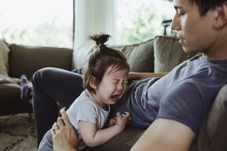 Father on paternity leave looking at male toddler crying in living room