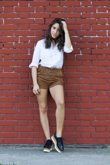 Full length portrait of young woman standing against brick wall
