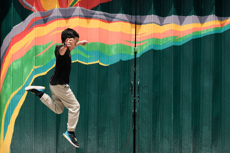 Side view of boy jumping by metallic gate