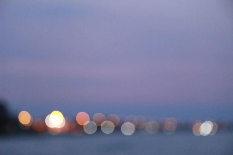 Defocused image of illuminated lights in sea against sky