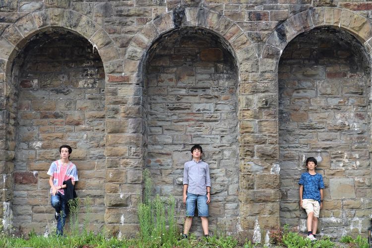 Full length of teenage brothers standing under arches against historic wall