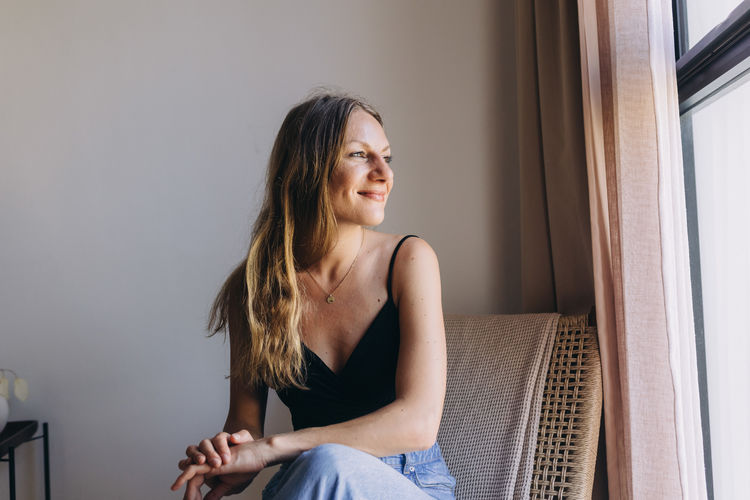 Low angle view portrait of woman sitting by the window on a woven chair 