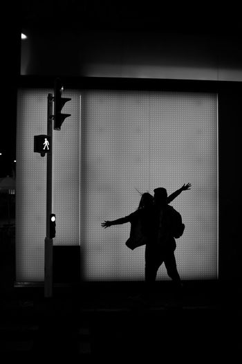 Silhouette man carrying woman on road against wall