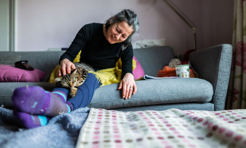 Woman petting cat while sitting on sofa at home