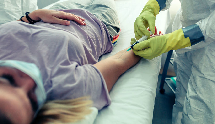 Midsection of doctor injecting patient on bed in hospital