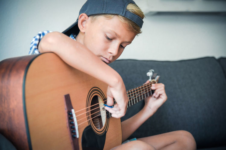 Boy playing guitar while sitting on sofa at home