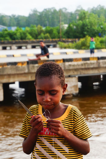 Boy holding plastic wire and knife by river