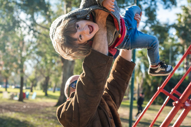 Full length of child boy on field in park being raised up by adult man