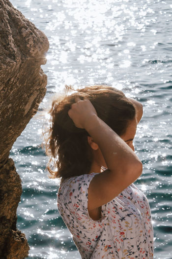 Side view of woman with hand in hair standing against sea