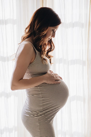 Side view of pregnant woman standing by window