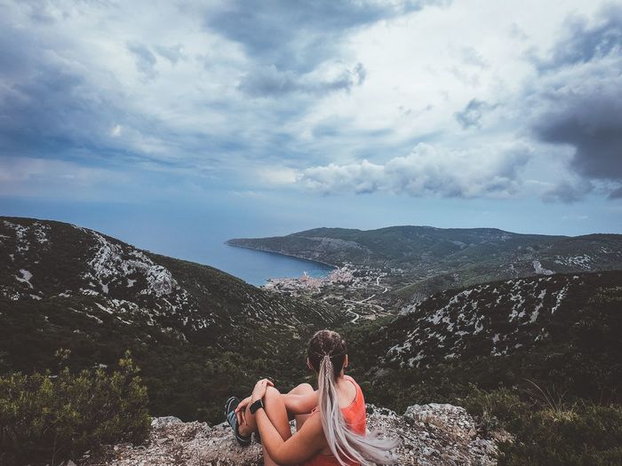 Rear view of female hiker sitting on mountain against sky