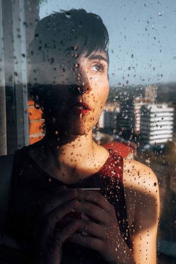 Portrait of woman seen through wet window in rainy season