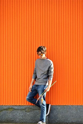 Teenage boy standing by orange wall