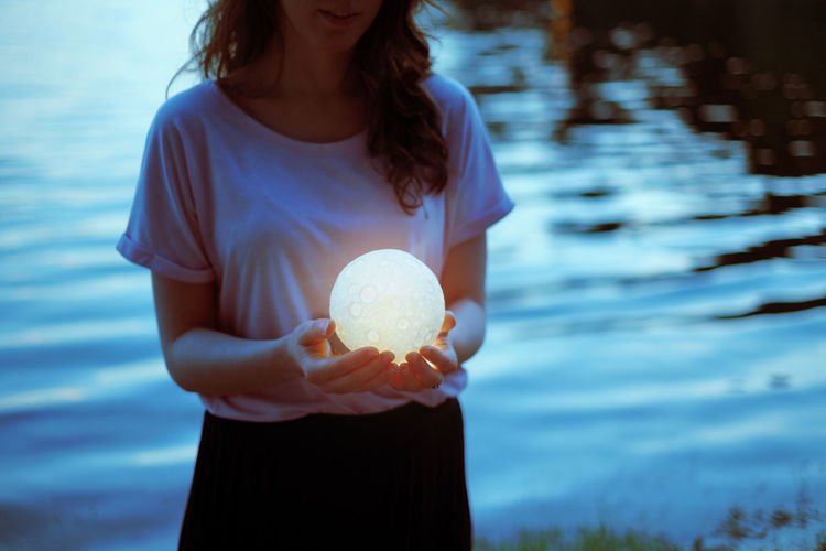 Midsection of woman holding sphere shape lamp