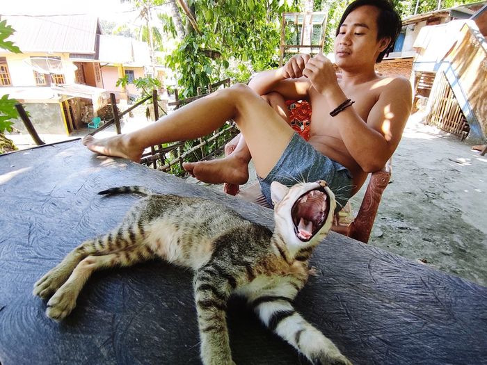 A man relaxing in front of a house with a cat