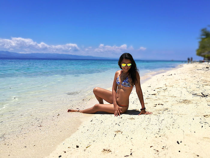 Woman in bikini and sunglasses sitting at beach