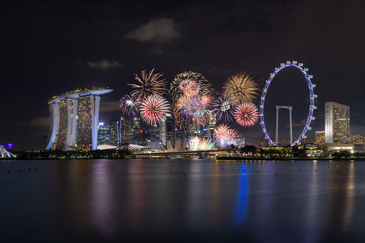 Firework display over illuminated city against sky at night