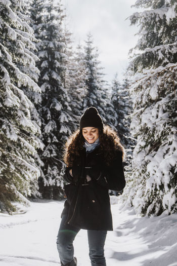 Smiling young woman in warm clothing standing amidst trees on snowy field