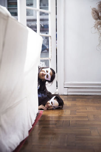 Portrait of sisters wearing eye masks peeking by sofa at home