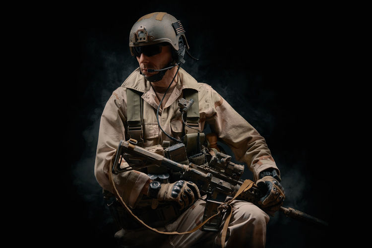 Man wearing helmet holding rifle against black background