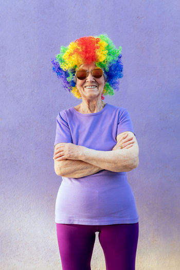 Portrait of smiling man with multi colored hair standing against gray background