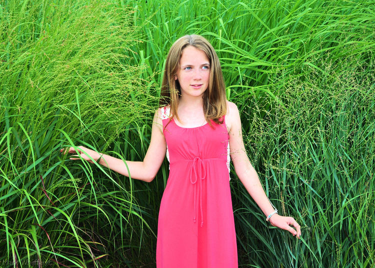Teenage girl looking away while standing against plants on field