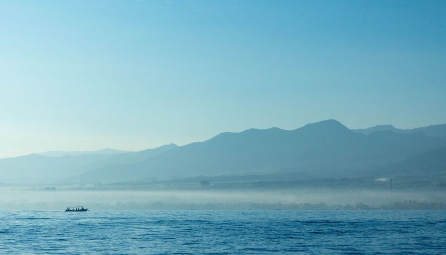 Scenic view of sea and mountains against clear blue sky